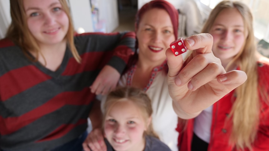 Woman and three girls standing close and smiling as the woman holds a red dice towards the camera.