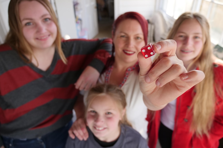 Woman and three girls standing close and smiling as the woman holds a red dice towards the camera.