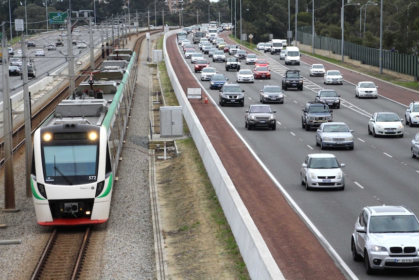 A train runs along the railway line in between traffic on the Mitchell Freeway.