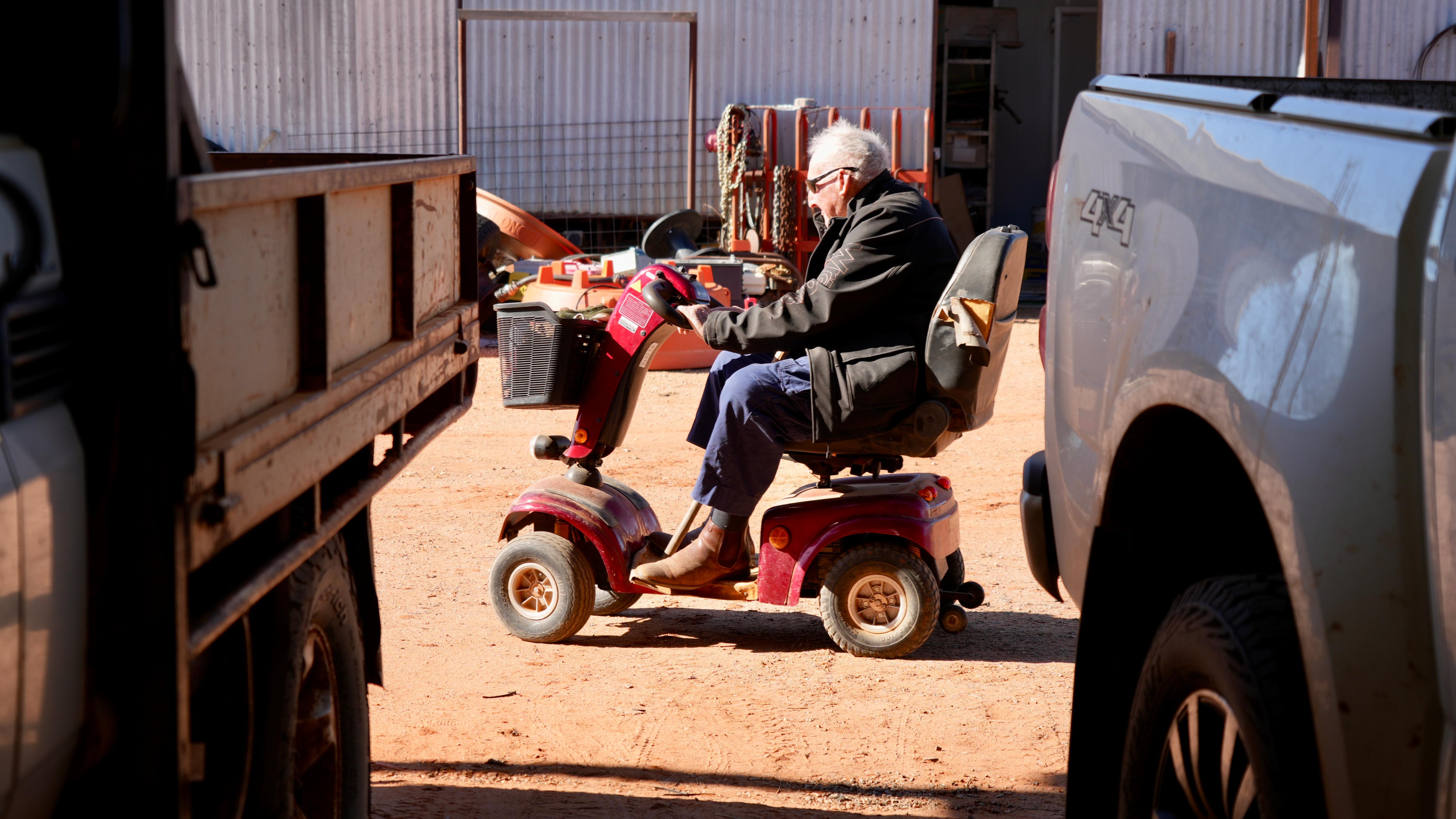 a man in blue pants, black jacket and sunglasses driving a red gopher between two vehicles 