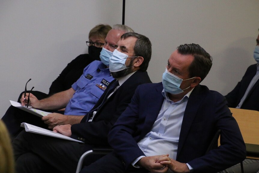 Three men and a woman sit on a row of seats in an office room, wearing face masks.