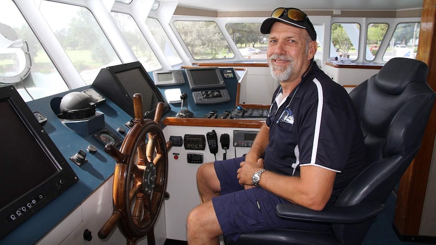 A man sits in front of the steering wheel of a very large catamaran.