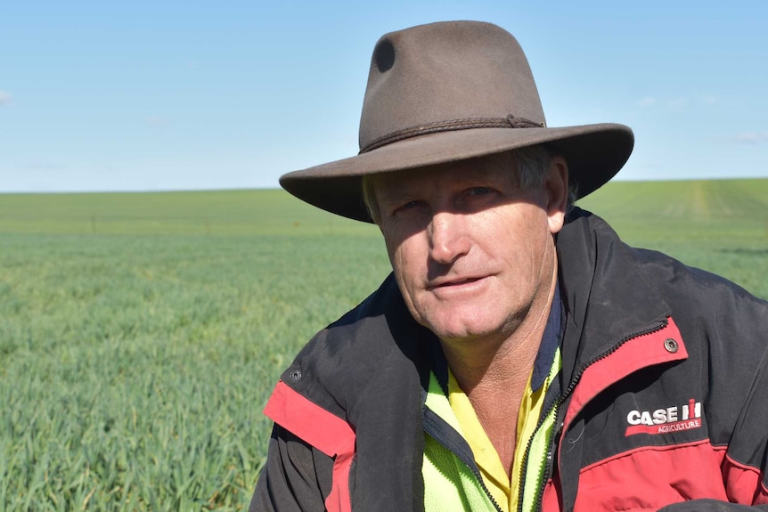 A man wearing an Akubra and fluoro looks down the camera with a pasture behind him.