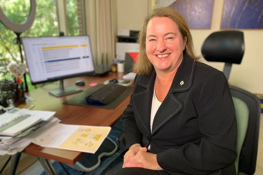 Mary Wooldridge sits at a desk with a computer in the background.