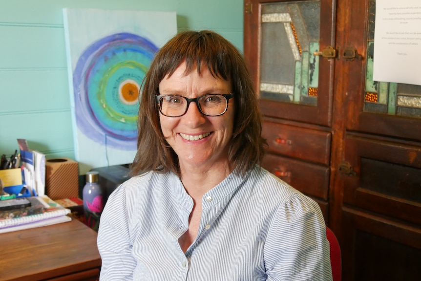 A woman with glasses smiles at the camera happily.