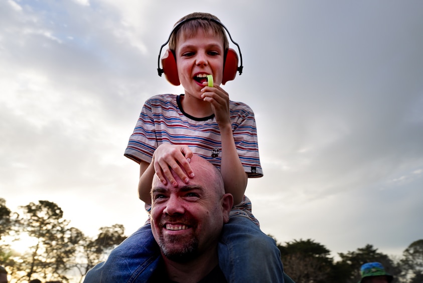 A young fan sits on his dad's shoulders with earmuffs on.
