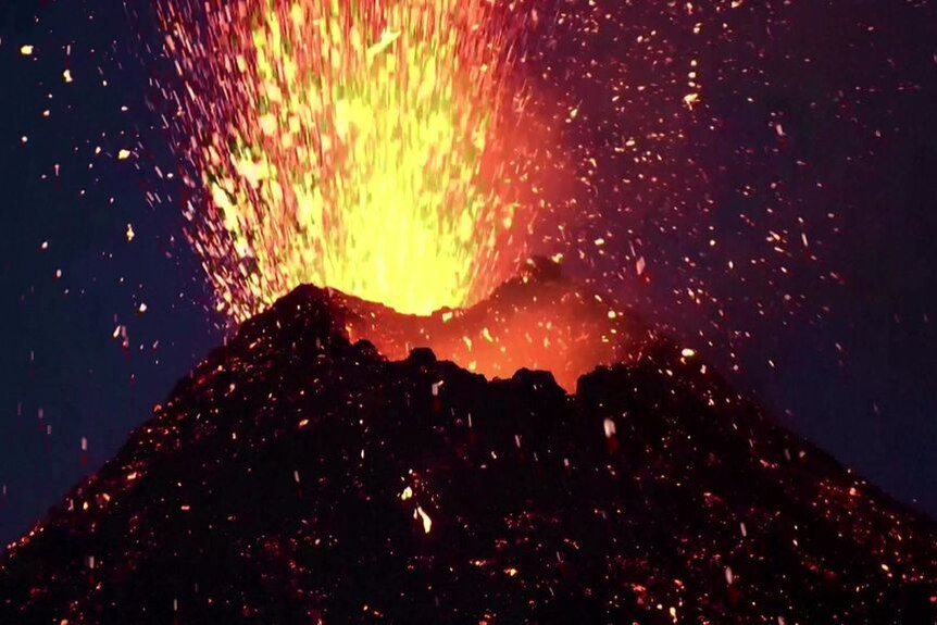 Lava spewing out of the funnel of a volcano at night.