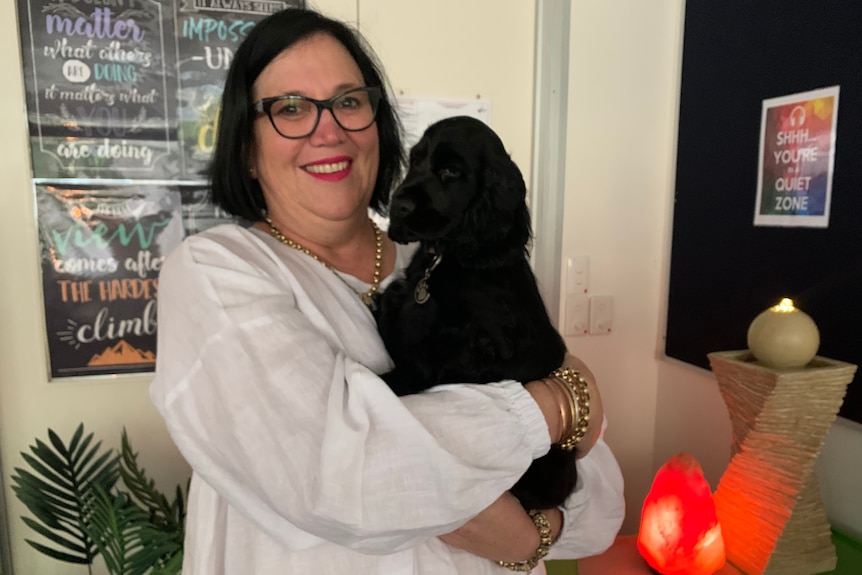 Support worker smiling holding black cocker spaniel puppy Luna in her arms.