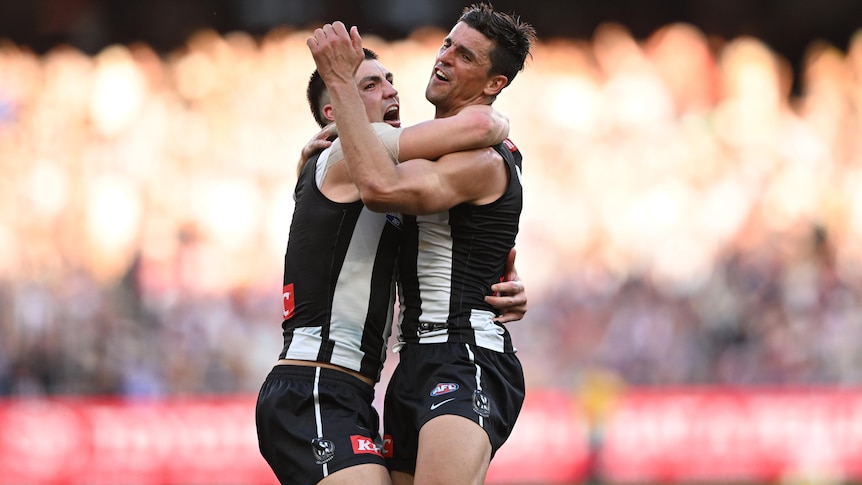 Two Collingwood AFL players embrace as they celebrate winning the grand final.