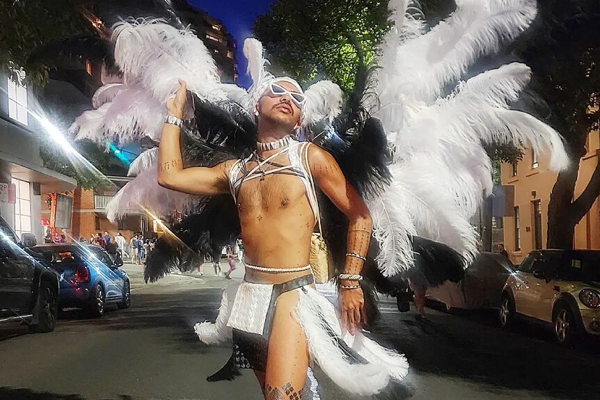 A fabulous bare-chested Chammoro Indigenous man stands in the Sydney Mardi Gras parade with large white and black feather wings.