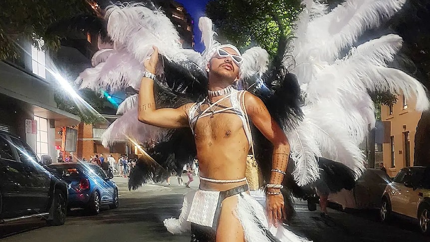 A fabulous bare-chested Chammoro Indigenous man stands in the Sydney Mardi Gras parade with large white and black feather wings