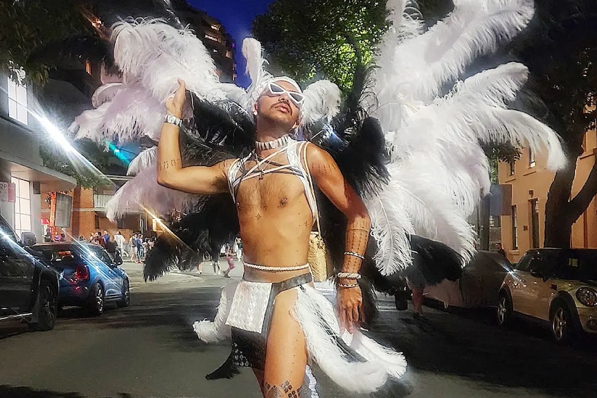 A fabulous bare-chested Chammoro Indigenous man stands in the Sydney Mardi Gras parade with large white and black feather wings