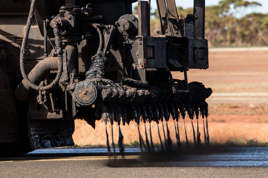 A close-up of a truck which is spraying a tar-like substance to resurface a runway.  