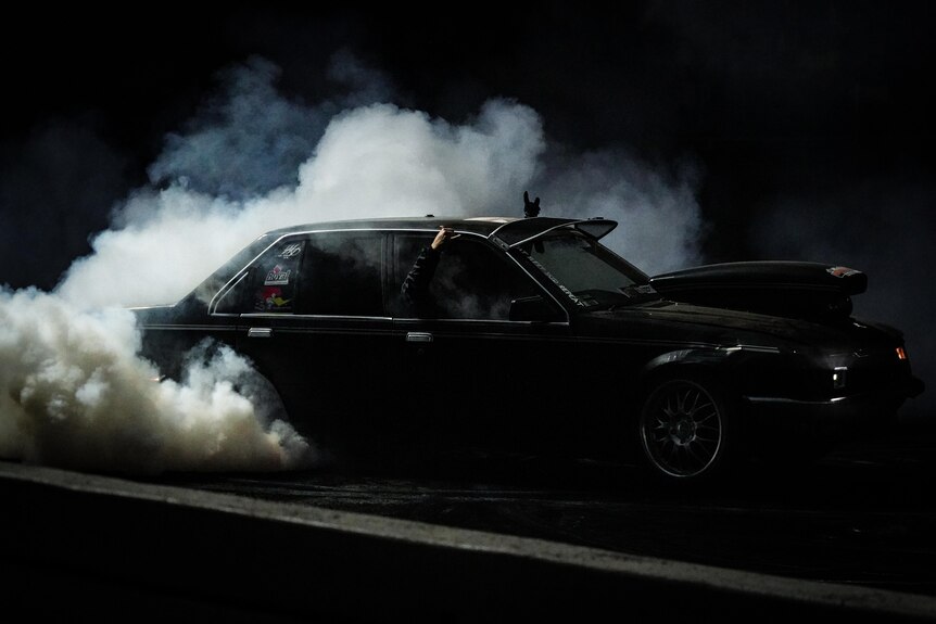 Smokes rises from a black vehicle doing a burnout