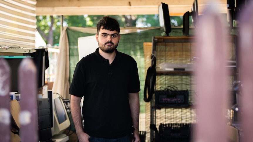 Man standing in an open garage full of old computer and electronics.