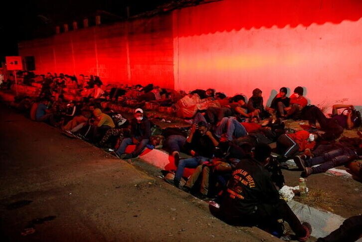 Migrants on the road in Vado Hondo where they rest at night, against a wall with red lighting.