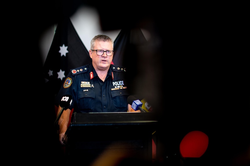 A police officer speaks at a media conference. He looks serious.