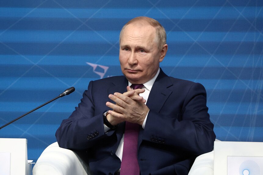 Vladimir Poutine assis sur une chaise blanche, les mains jointes.