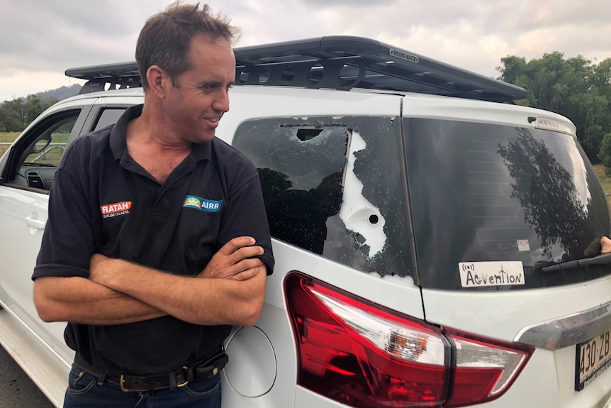 A man looks at his cracked window which has been shattered by large hailstones.