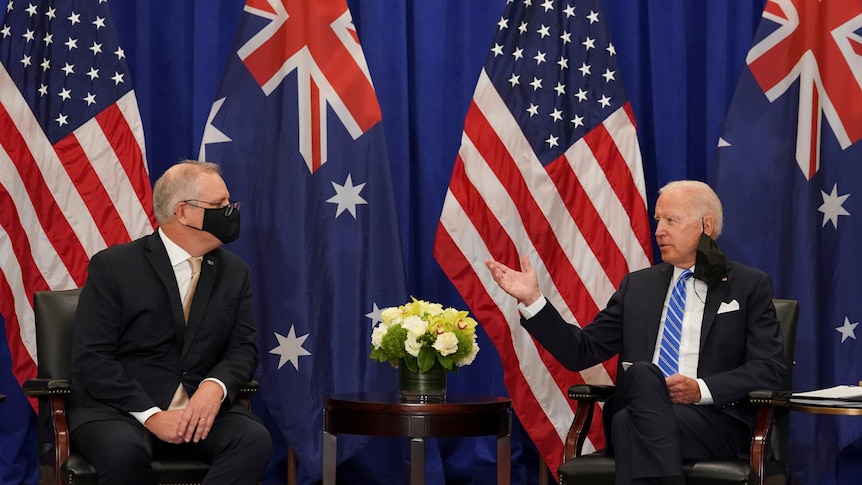 Scott Morrison and Joe Biden sit talking in front of US and Australian flags.
