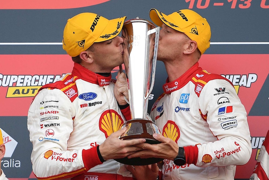 Two SuperCars drivers hold and kiss the Bathurst 1000 trophy on the victory podium.