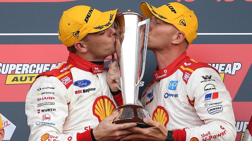 Two SuperCars drivers hold and kiss the Bathurst 1000 trophy on the victory podium.