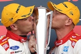 Two SuperCars drivers hold and kiss the Bathurst 1000 trophy on the victory podium.