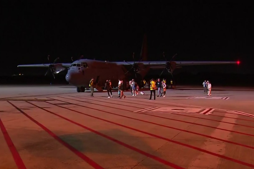 A large army plane sits on an airport tarmac as people walk away from it at night