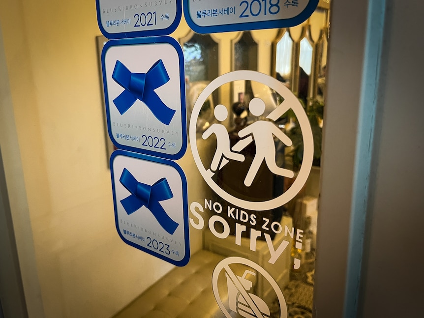 A sticker on a mirror reads NO KIDS ZONE, SORRY, next to a symbol with a line through two people