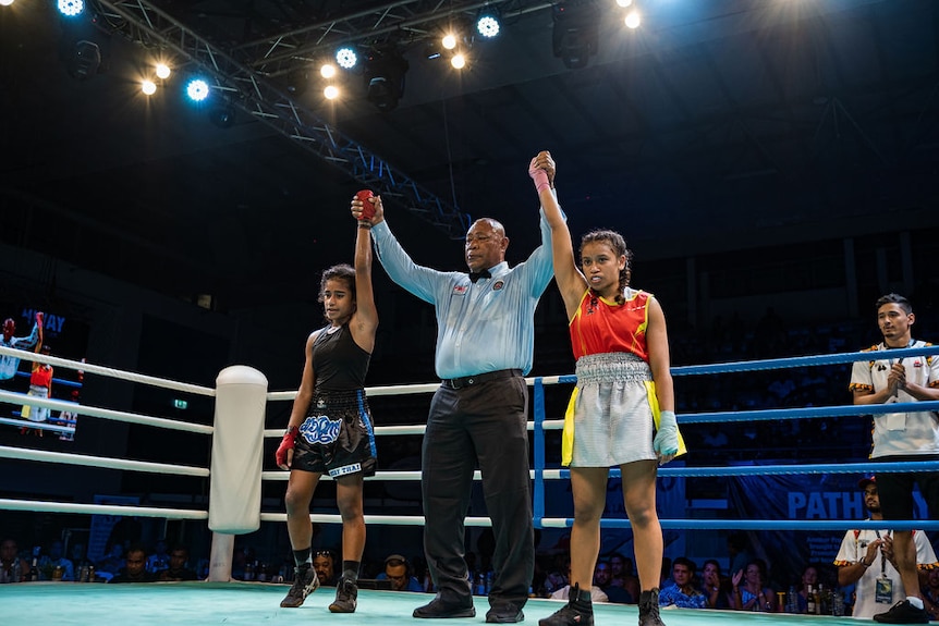 A referee holds the hands of two teenage boxers in the air to signal the end of a match.