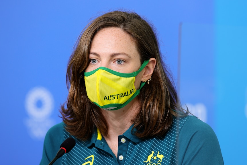Wearing a green and gold mask with AUSTRALIA printed on it, Cate Campbell sits in front of a microphone