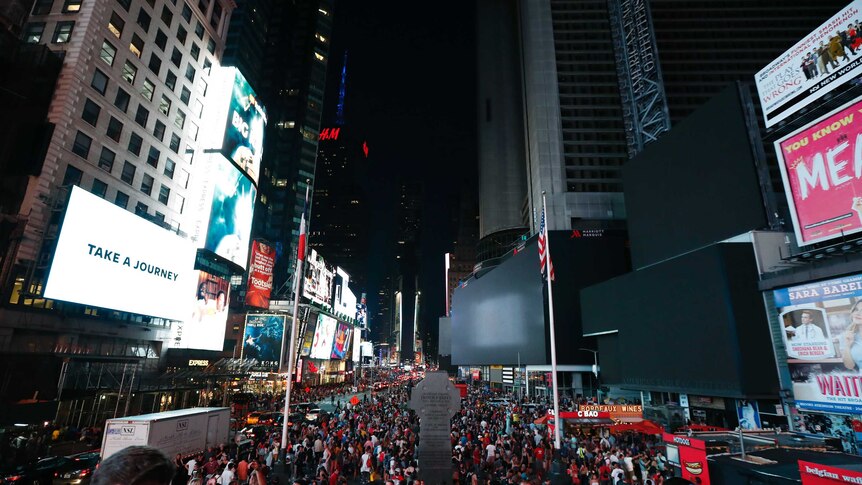 Hundreds of people mill about Times Square as the majority of the area is plunged into darkness without screens.