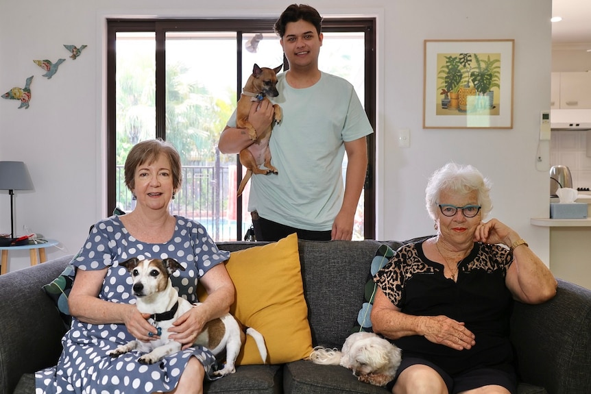 Three people sitting and standing inside a house holding their dogs.