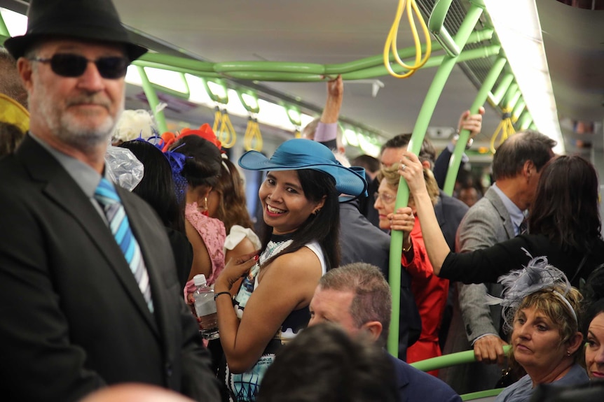 Smiling lady in fascinator in middle of crowded train.
