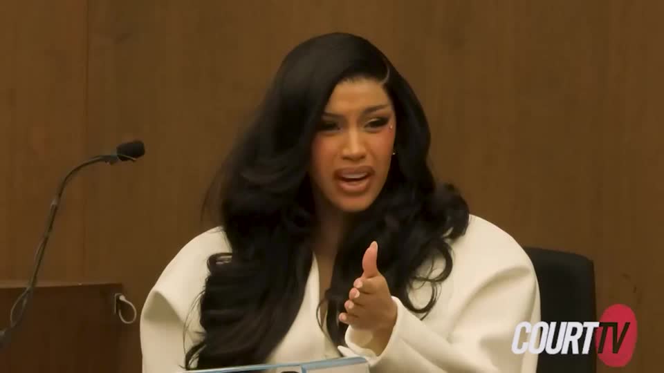 Cardi speaking in a witness box with a concerned expression and her hand out.
