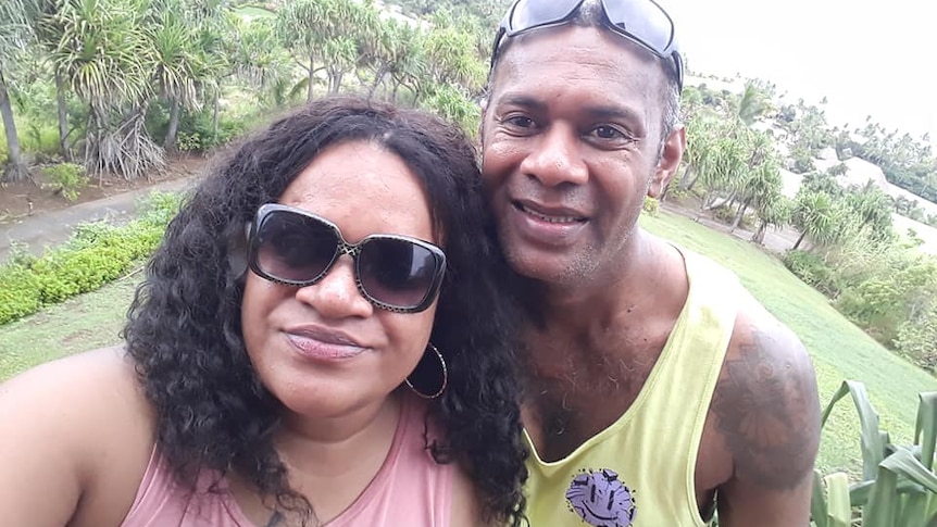 A Fijian couple smile in a selfie, surrounded by greenery.