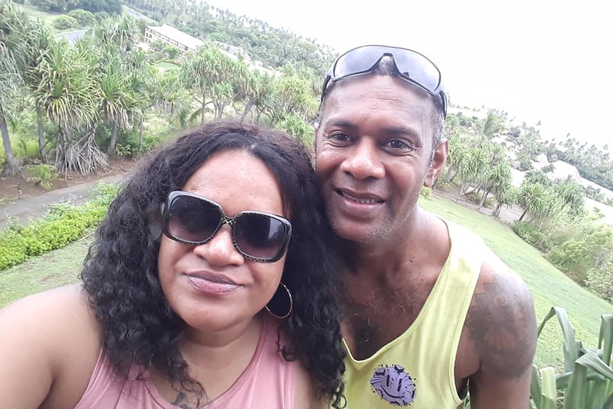 A Fijian couple smile in a selfie, surrounded by greenery.