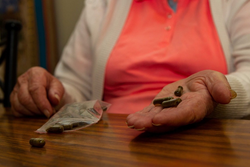 An elderly hand holds medicinal cannabis pills