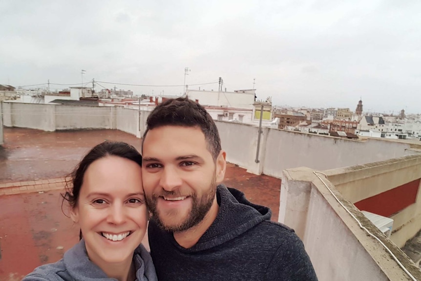 A couple pose on a roof top terrace with a cityscape in the background