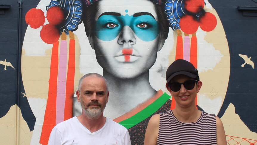 Close-up of Fin DAC and April standing in front of the face on the mural.