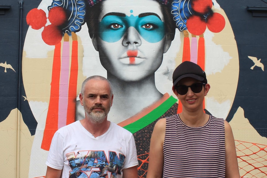 Close-up of Fin DAC and April standing in front of the face on the mural.
