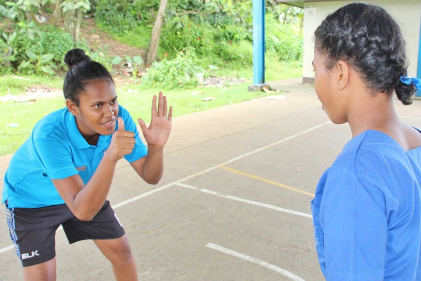 Tiyana crouches with her hands up in front of her while coaching a girl in a school uniform.