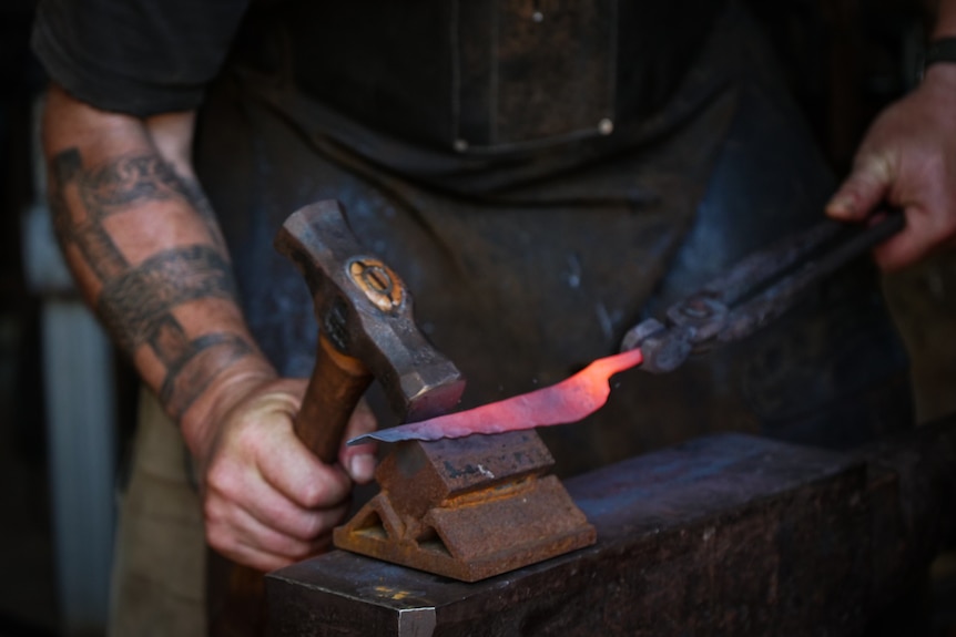 Close up of tattooed hand hammering a heated steel leaf