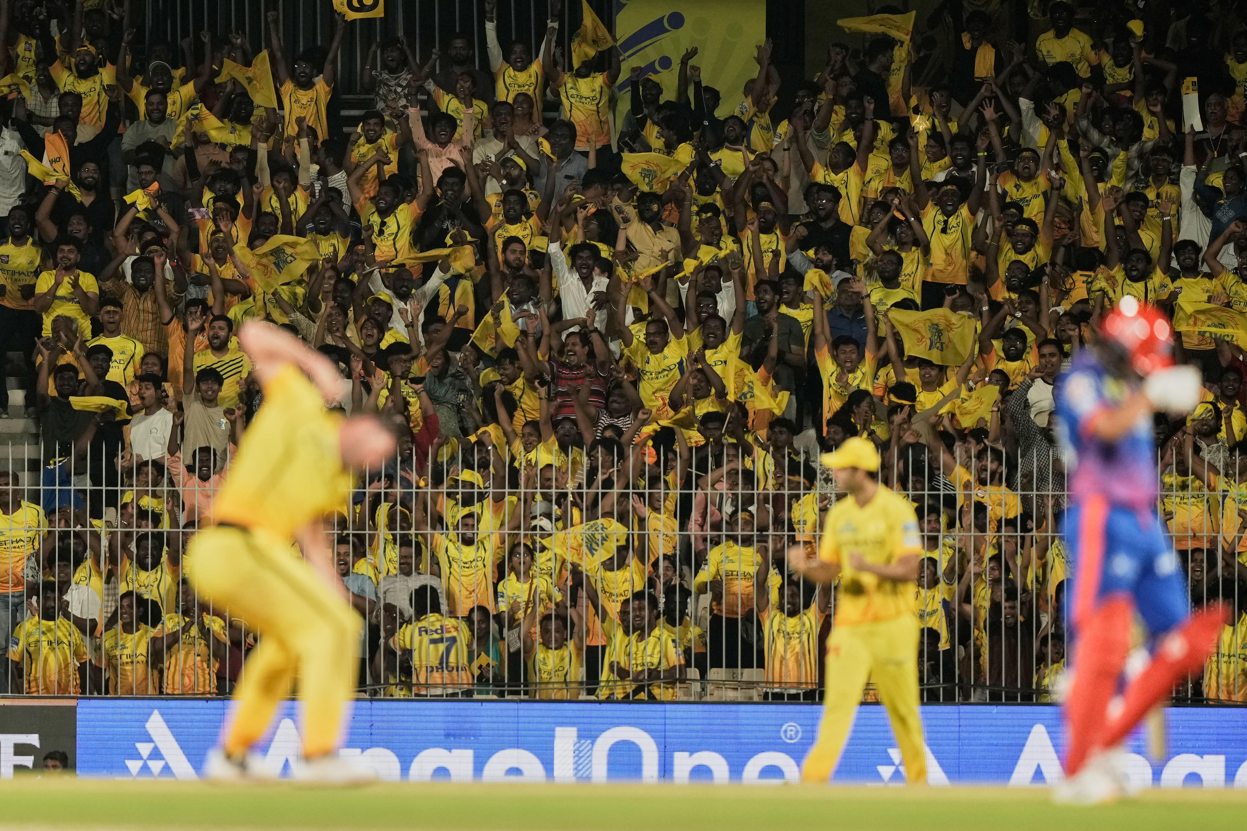 A picture of a bowler celebrating a wicket as a batter walks off, while a big group of fans in yellow cheer in the background.  