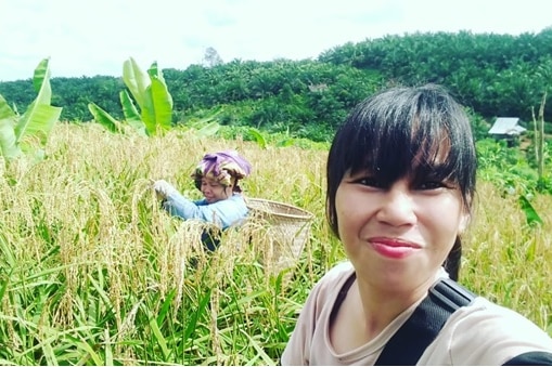 A woman taking photo in the rice field with a female farmer in the background.