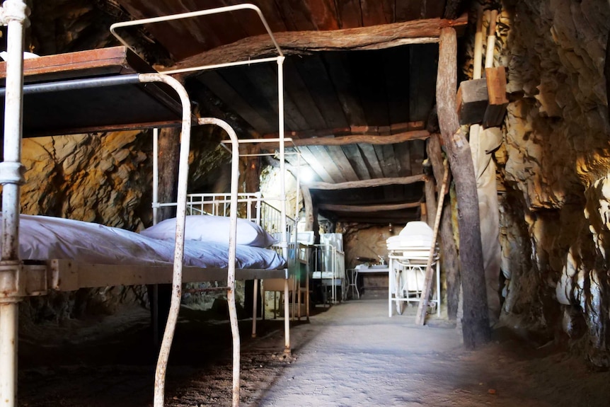 A tunnel, underground, filled with old hospital beds. The walls are rock.