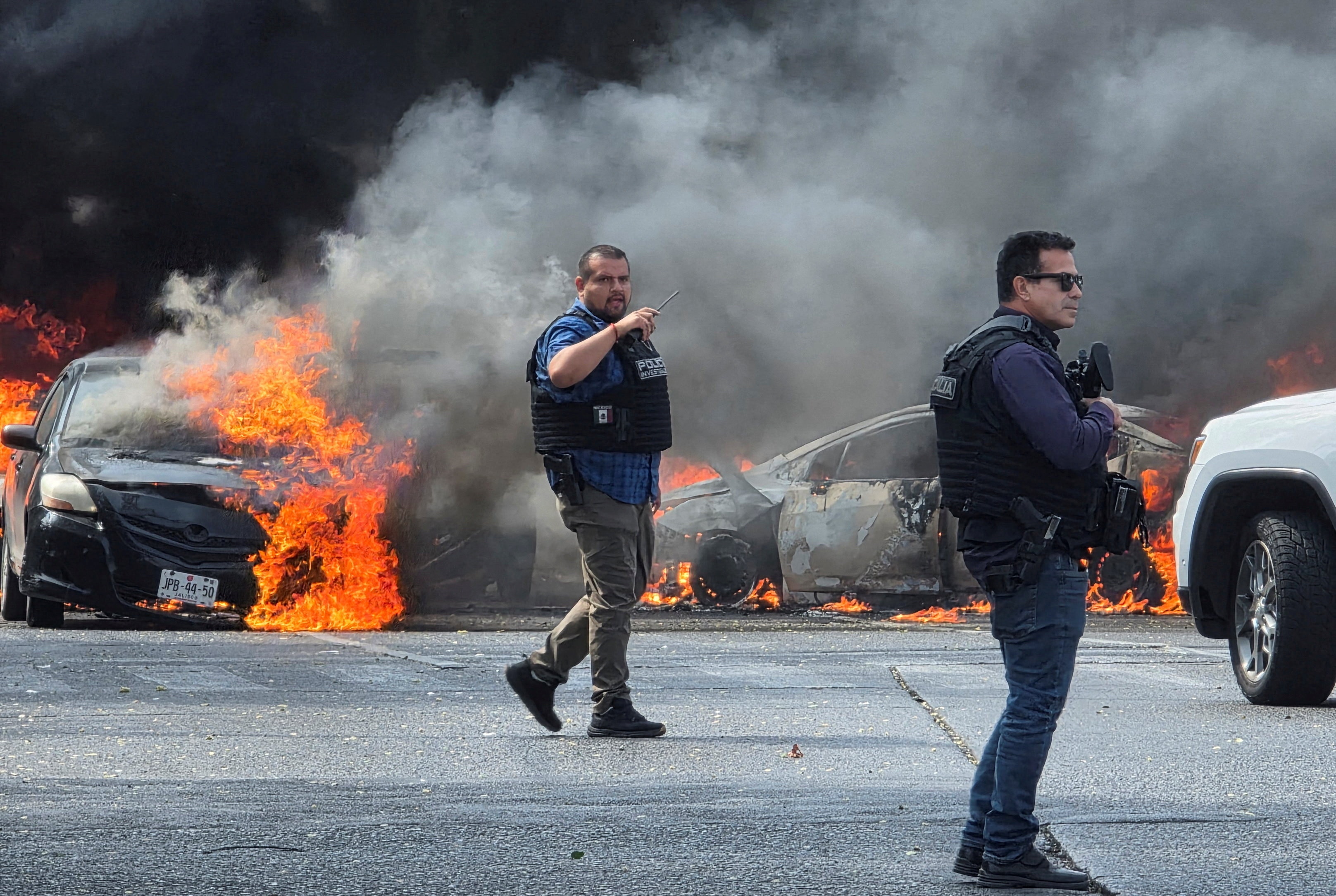 police officiers stand in front of two cars with orange flames coming from them.
