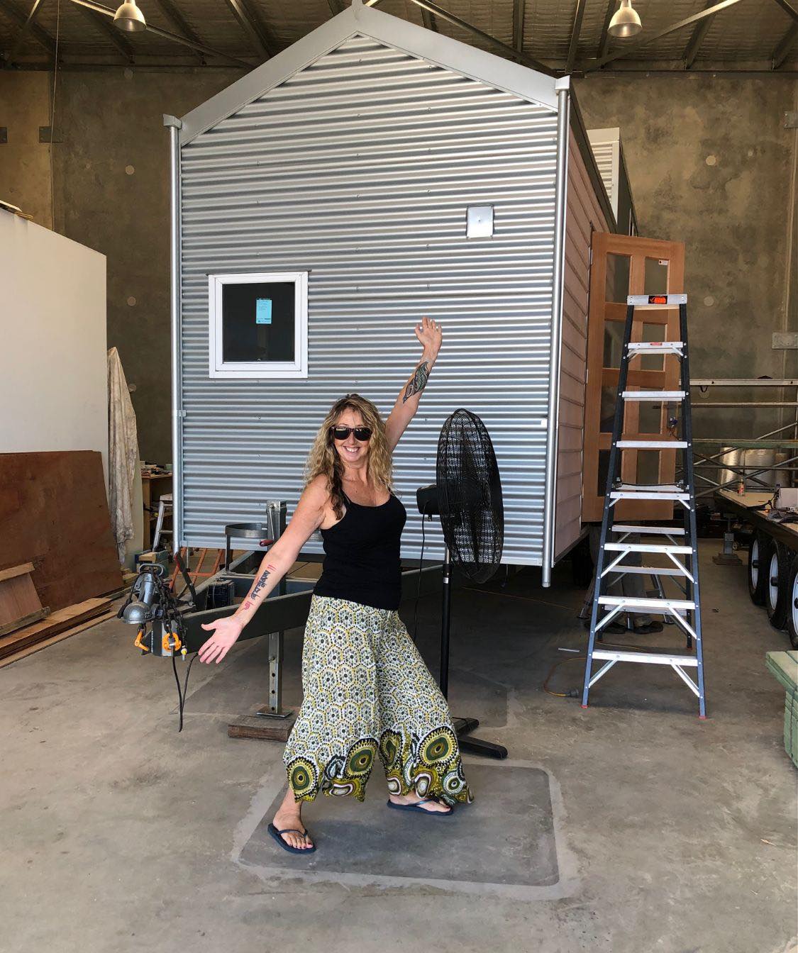 She wears a singlet and spreads her arms, showing off the tiny house behind her