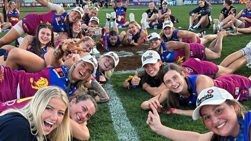 A selfie taken by the team coach who is lying down with the players all lined up behind him on the pitch.