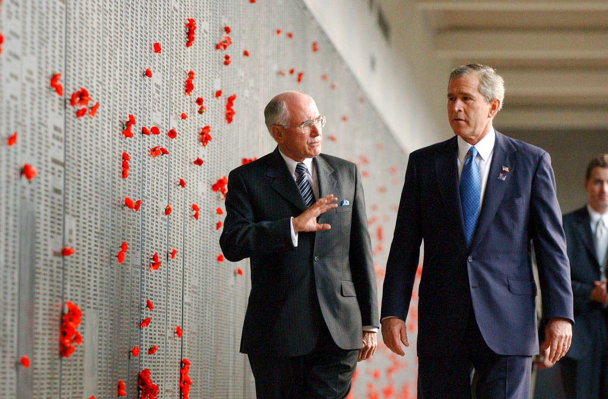Bush and Howard walk beside a memorial wall marked with poppy flowers.